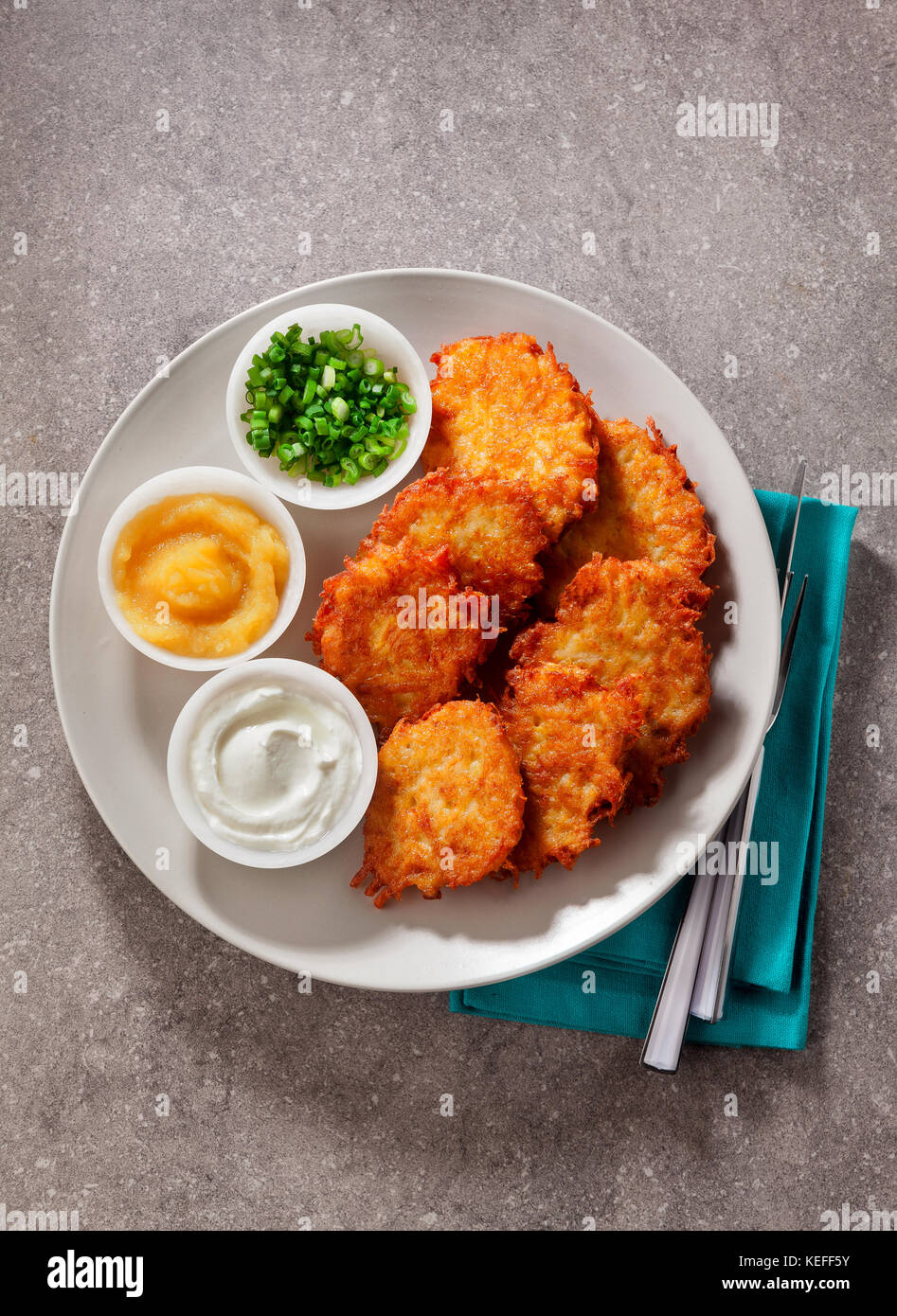 Kartoffelpuffer, latkes oder Boxty und Saucen aus Sauerrahm, Joghurt, Apfelmus und fein gehackten Frühlingszwiebeln auf grauem Stein Hintergrund Stockfoto