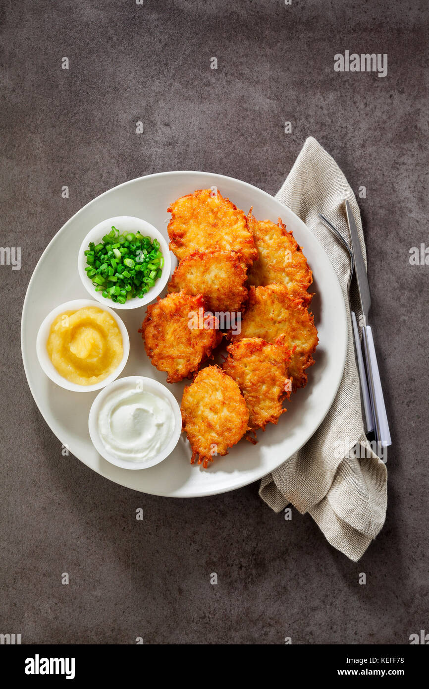 Kartoffelpuffer, latkes oder Boxty und Saucen aus Sauerrahm, Joghurt, Apfelmus und fein gehackten Frühlingszwiebeln auf grauem Stein Hintergrund Stockfoto