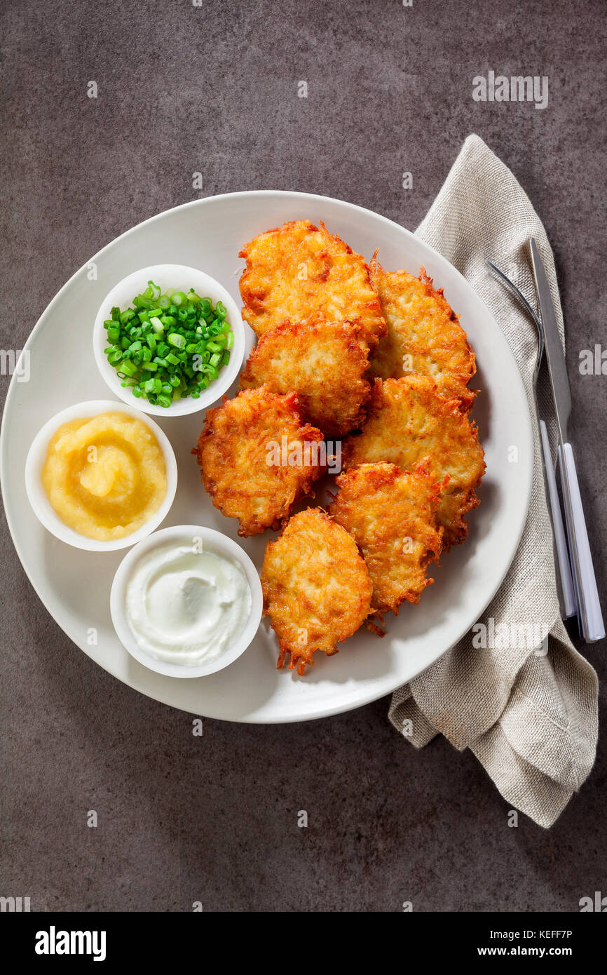 Kartoffelpuffer, latkes oder Boxty und Saucen aus Sauerrahm, Joghurt, Apfelmus und fein gehackten Frühlingszwiebeln auf grauem Stein Hintergrund Stockfoto