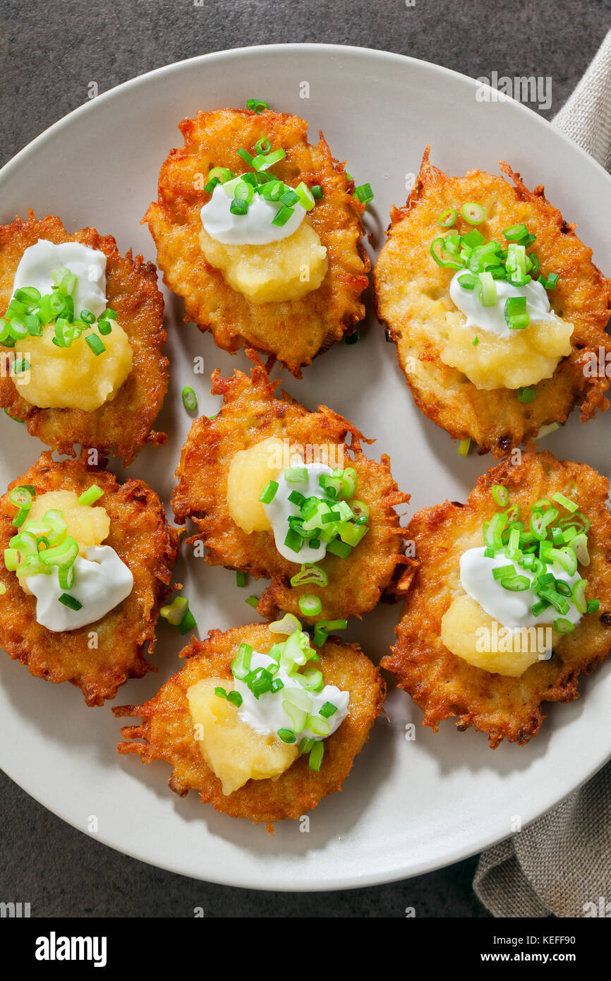 Kartoffelpuffer, latkes oder Boxty und Saucen aus Sauerrahm, Joghurt, Apfelmus und fein gehackten Frühlingszwiebeln auf grauem Stein Hintergrund Stockfoto