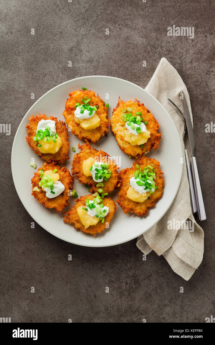 Kartoffelpuffer, latkes oder Boxty und Saucen aus Sauerrahm, Joghurt, Apfelmus und fein gehackten Frühlingszwiebeln auf grauem Stein Hintergrund Stockfoto
