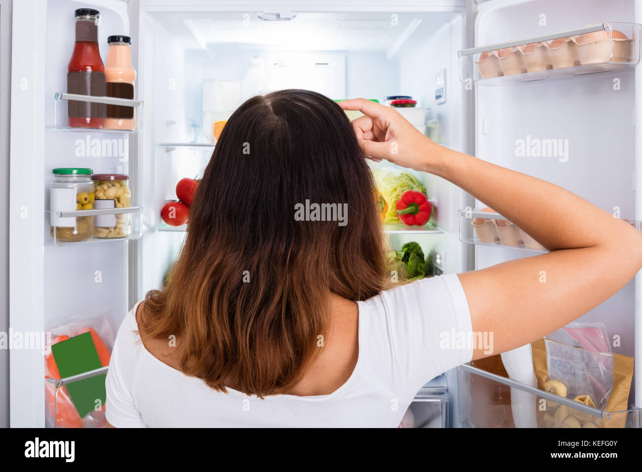 Ansicht der Rückseite des verwirrten Frau für Essen im Kühlschrank suchen Stockfoto