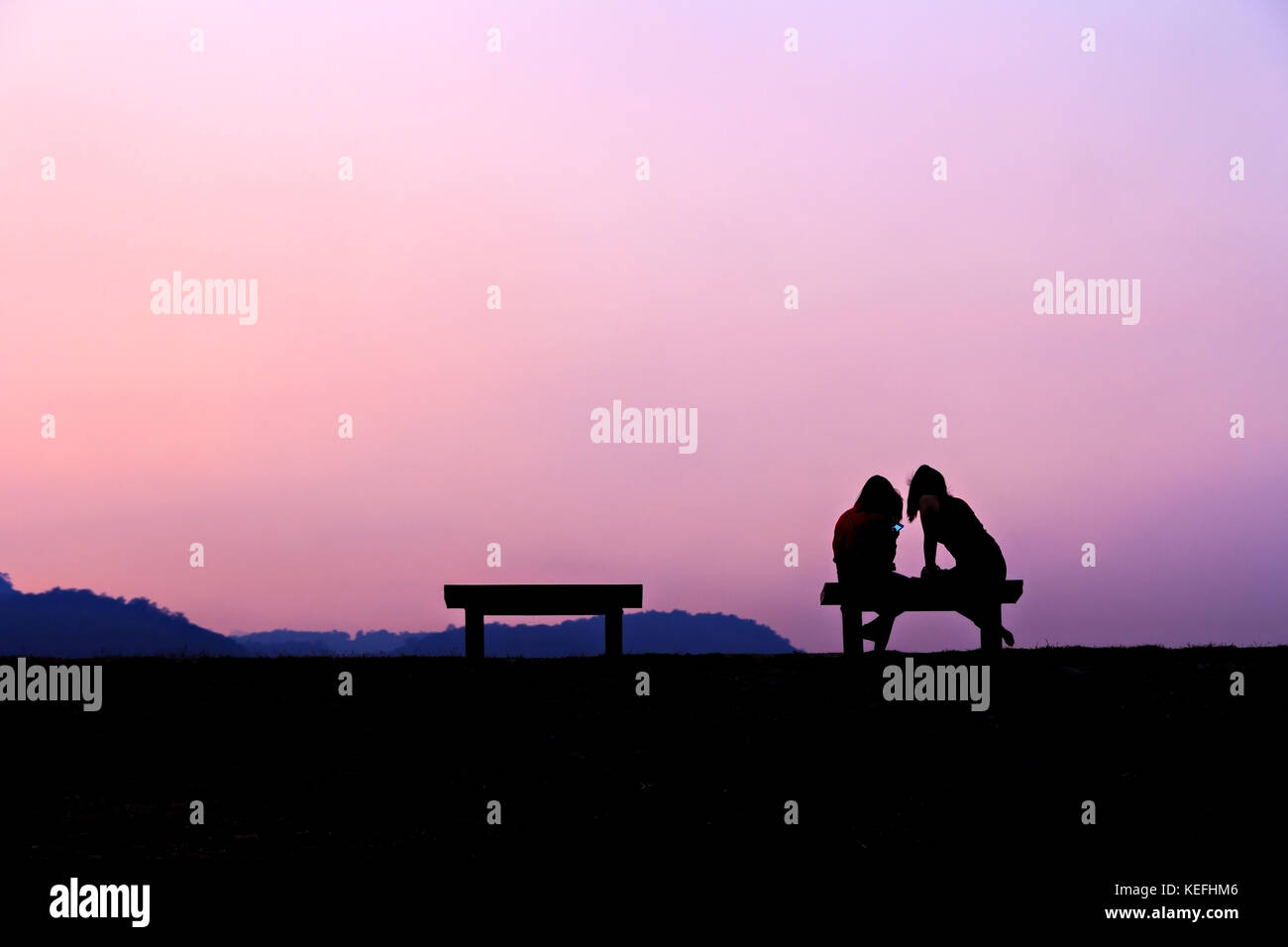 Silhouette von Mädchen sitzt auf der Bank in der Abenddämmerung Stockfoto