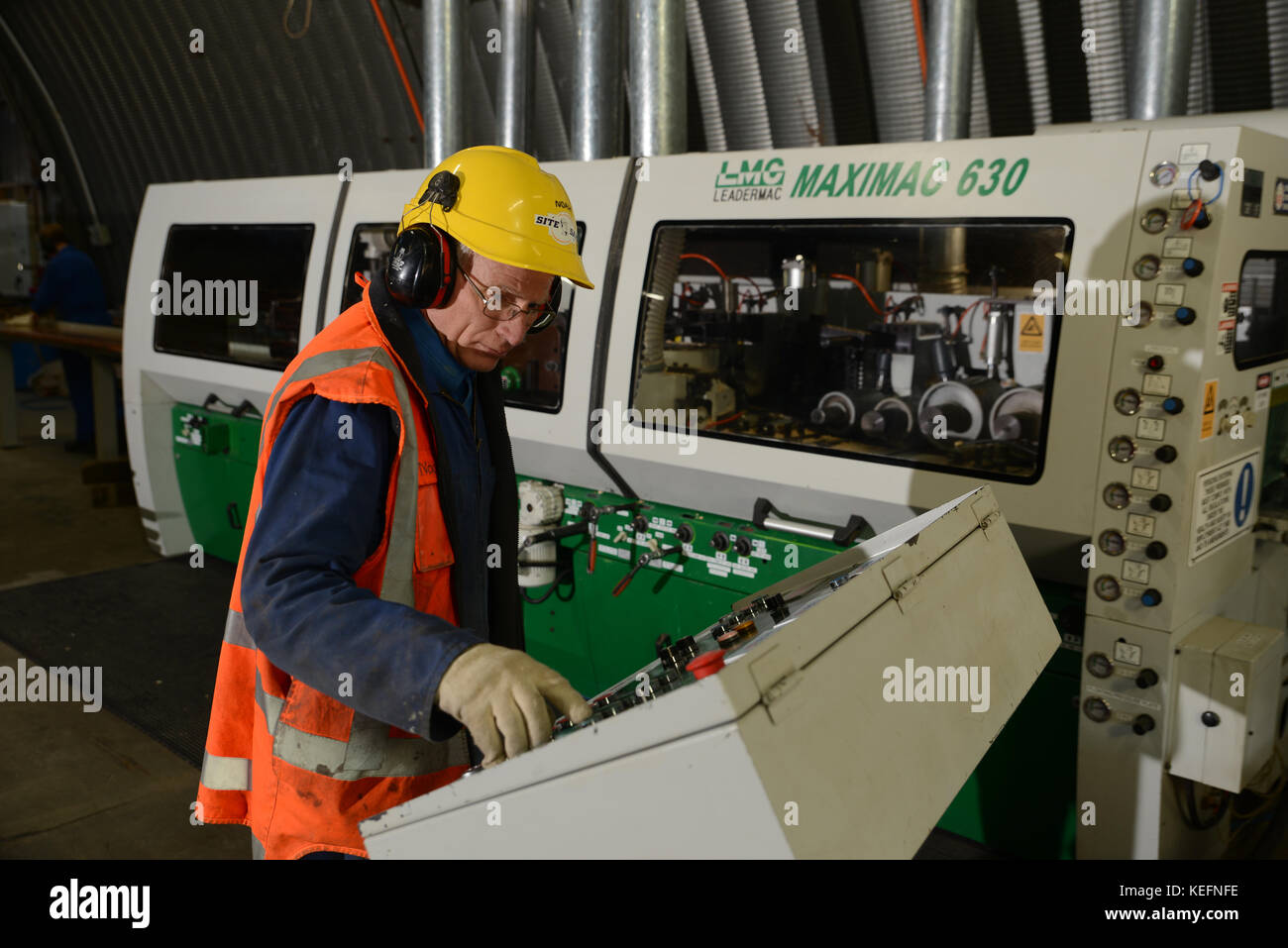 Arbeitnehmer mit einem vier sider Maschine ebene raue Kanten von vier Seiten von großen Kiefer Dielen in einer Holz verarbeitenden Fabrik in der Nähe von Greymouth, Neuseeland Stockfoto