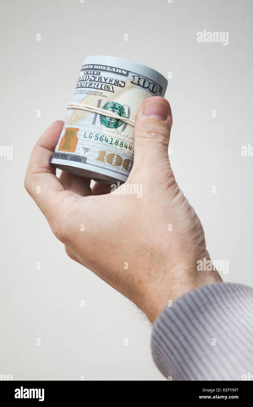 Rolle der neuen Hundert Dollar Noten in männlicher Hand über graue Wand Stockfoto