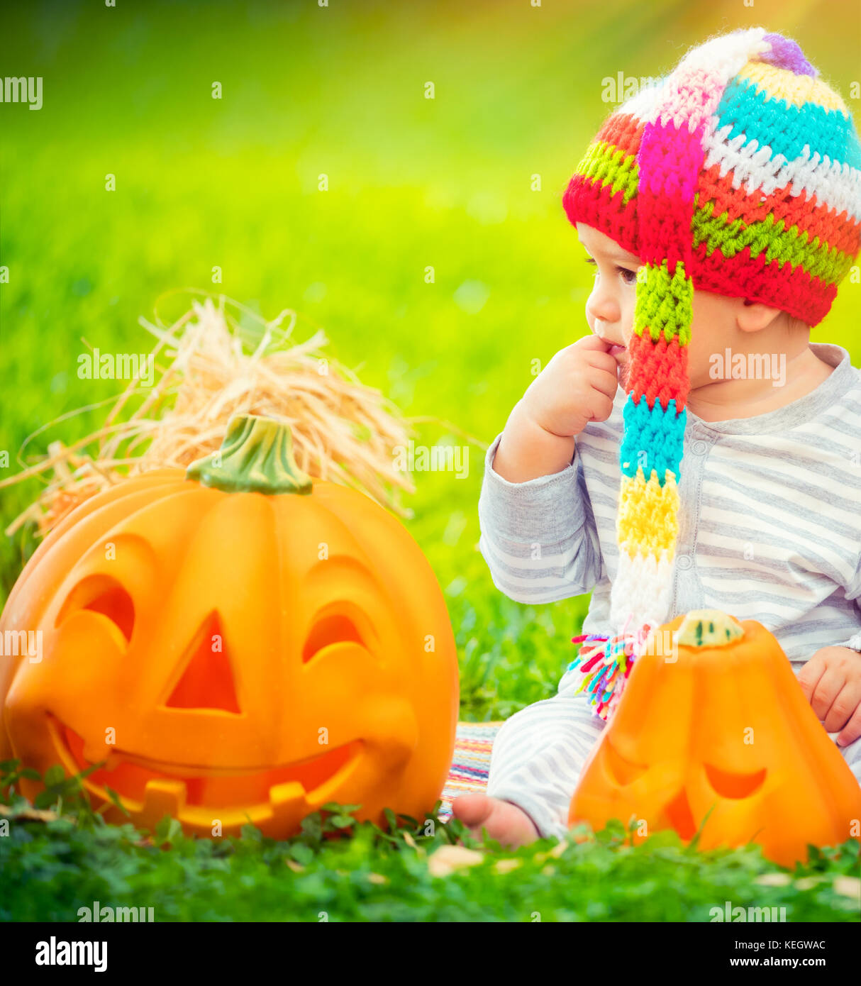 Porträt eines kleinen hübschen Kind sitzen auf der grünen Wiese in der Nähe von zwei süße Kürbisse mit geschnitzten Gesichtern, feiern Halloween Urlaub Stockfoto