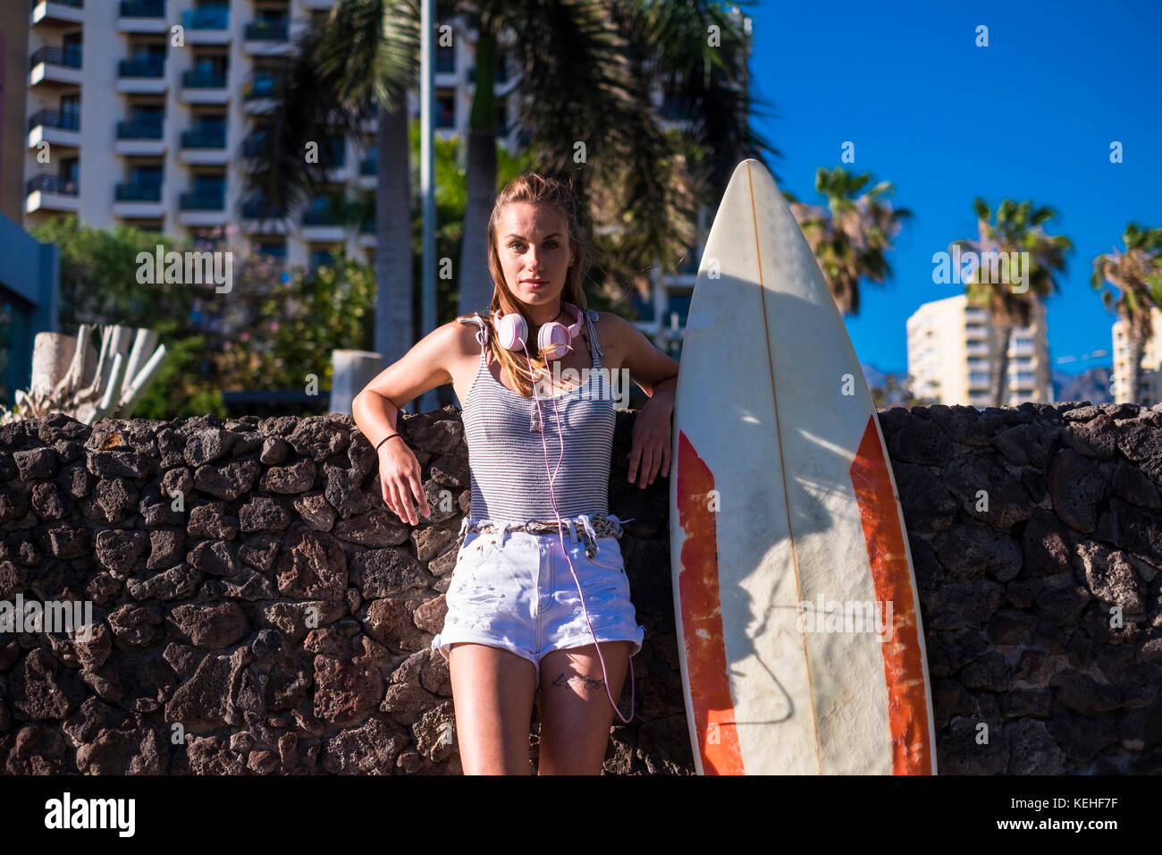 Kaukasische Frau, die sich an einer Steinwand neben dem Surfbrett lehnte Stockfoto