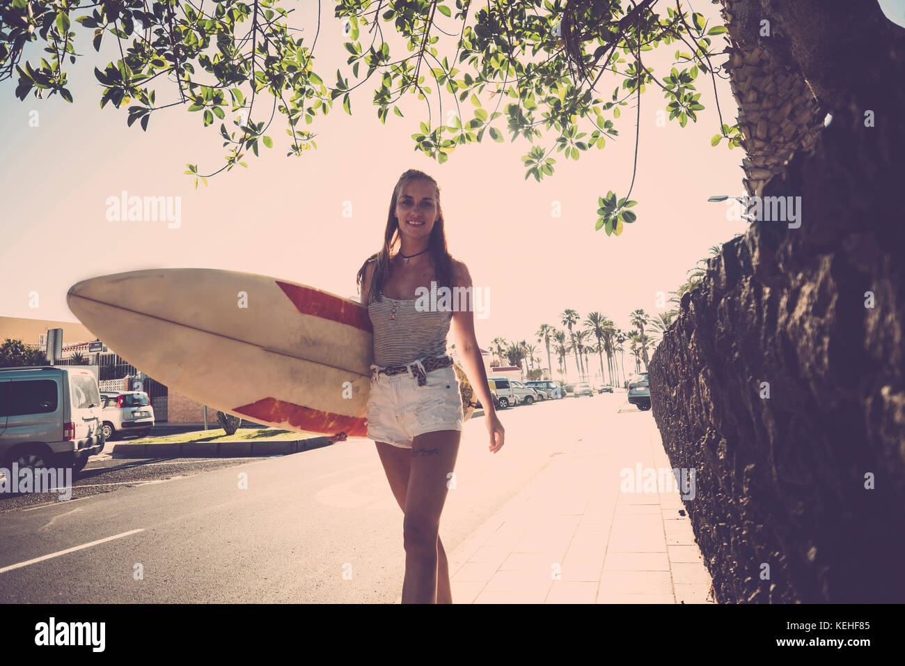 Kaukasische Frau, die auf dem Bürgersteig mit Surfbrett geht Stockfoto