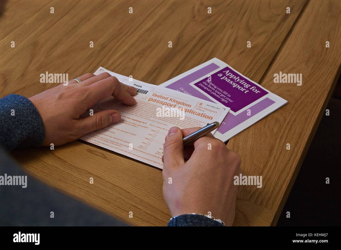 Blick auf die Hände des Menschen Ausfüllen britischen Reisepass Antragsformular auf Tabelle mit anweisende Broschüre Stockfoto