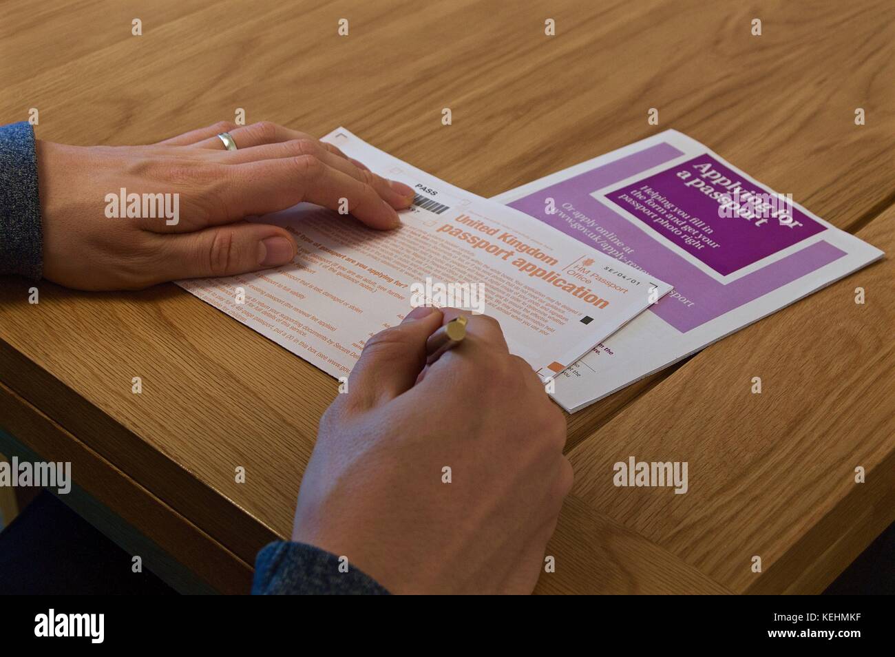 Blick auf die Hände des Menschen Ausfüllen britischen Reisepass Antragsformular auf Tabelle mit anweisende Broschüre Stockfoto