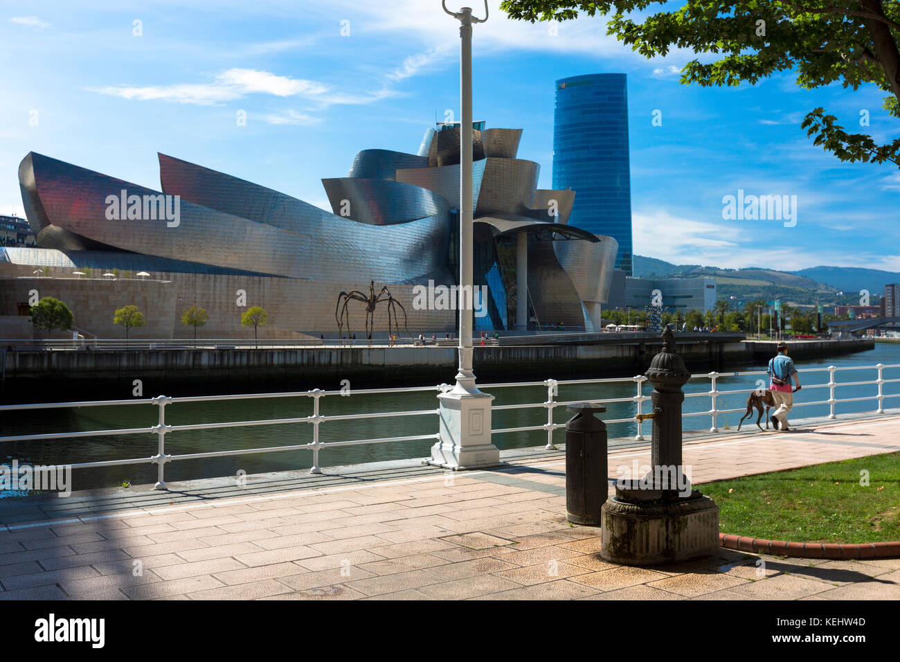 Mann, der Hund geht, hat am Guggenheim Museum des Architekten Frank Gehry über den Fluss Nervion in Bilbao, Baskenland, Spanien, vorbeigelaufen Stockfoto