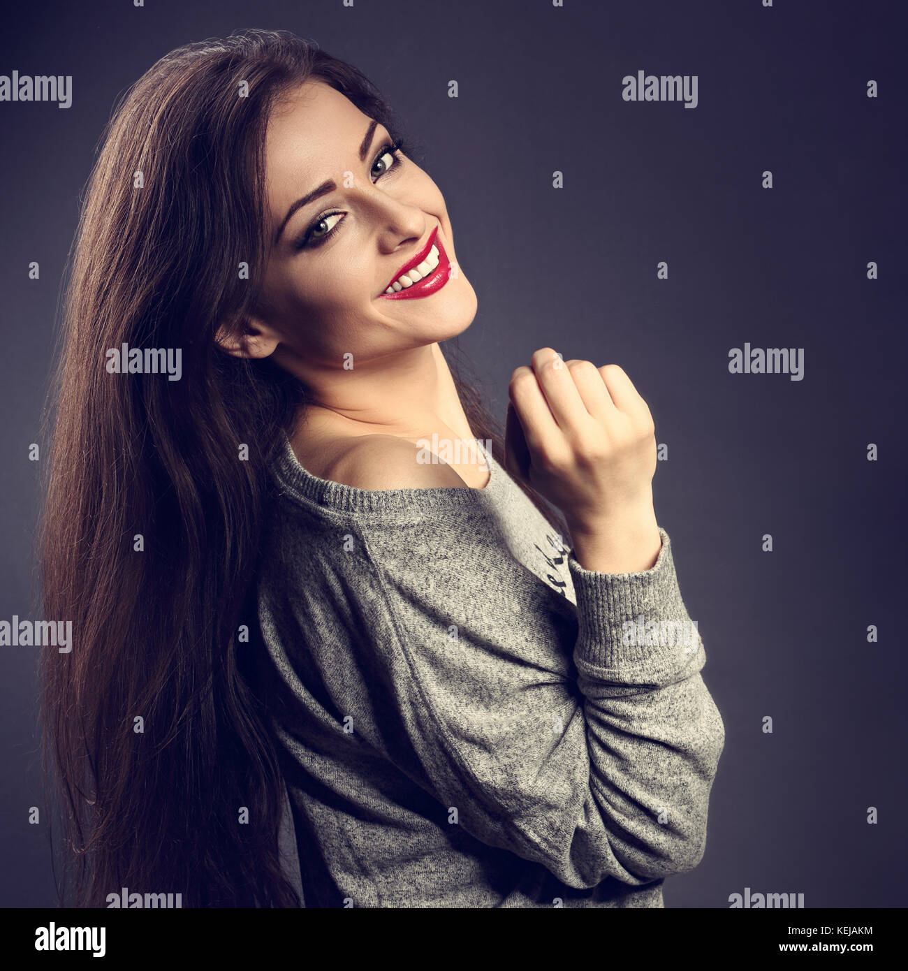 Gerne schöne Brünette Frau mit langem Haar style in Grau mode Pullover mit toothy Lächeln auf dunklen Schatten Hintergrund. closeup getönten Portr Stockfoto