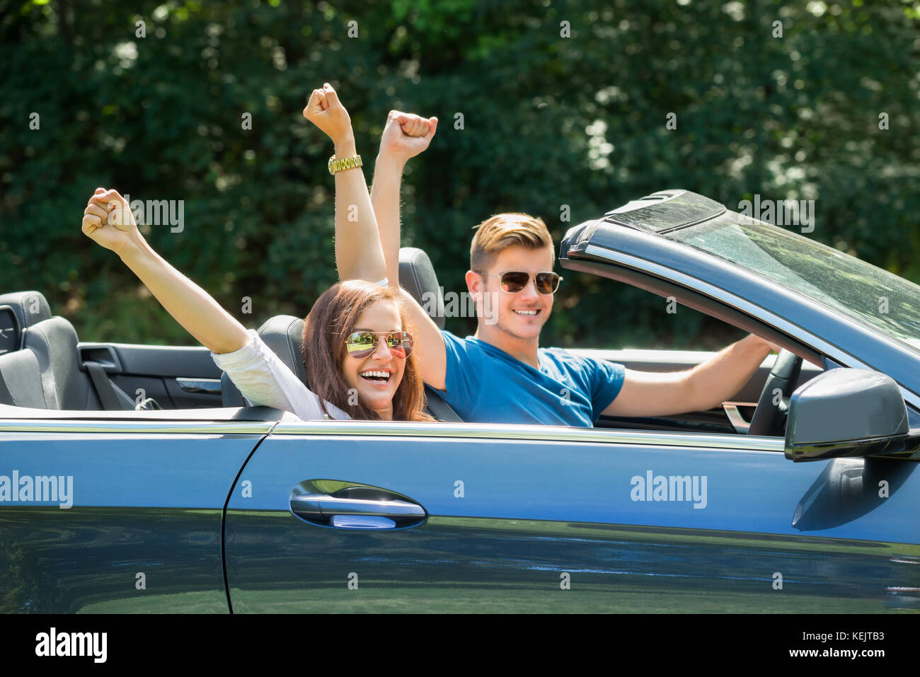 Glückliches Paar sitzen in einem Auto mit Sonnenbrille die Arme heben Stockfoto