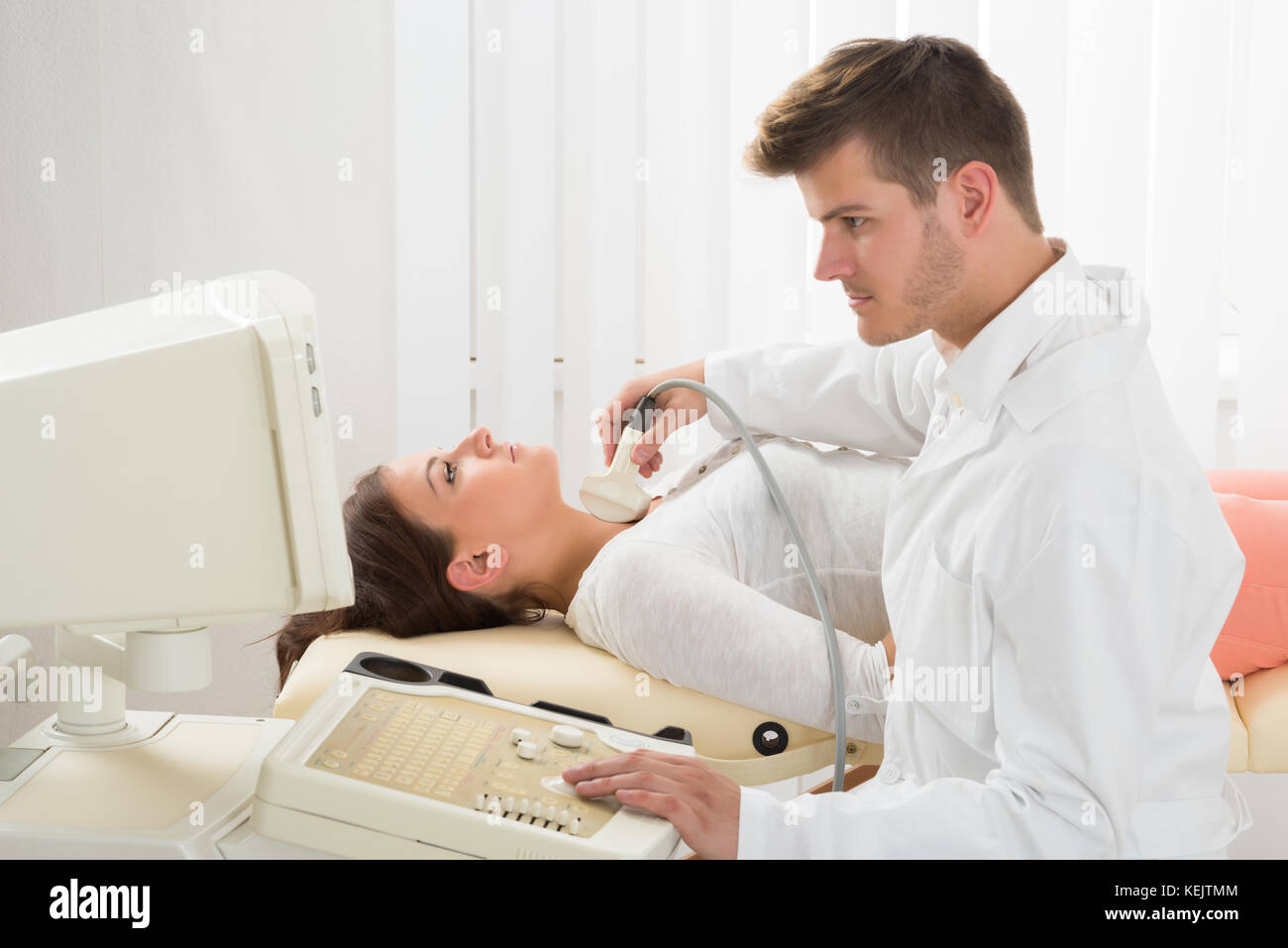 Ein hübscher Arzt über ein Ultraschallgerät auf der Kehle einer Patientin Stockfoto