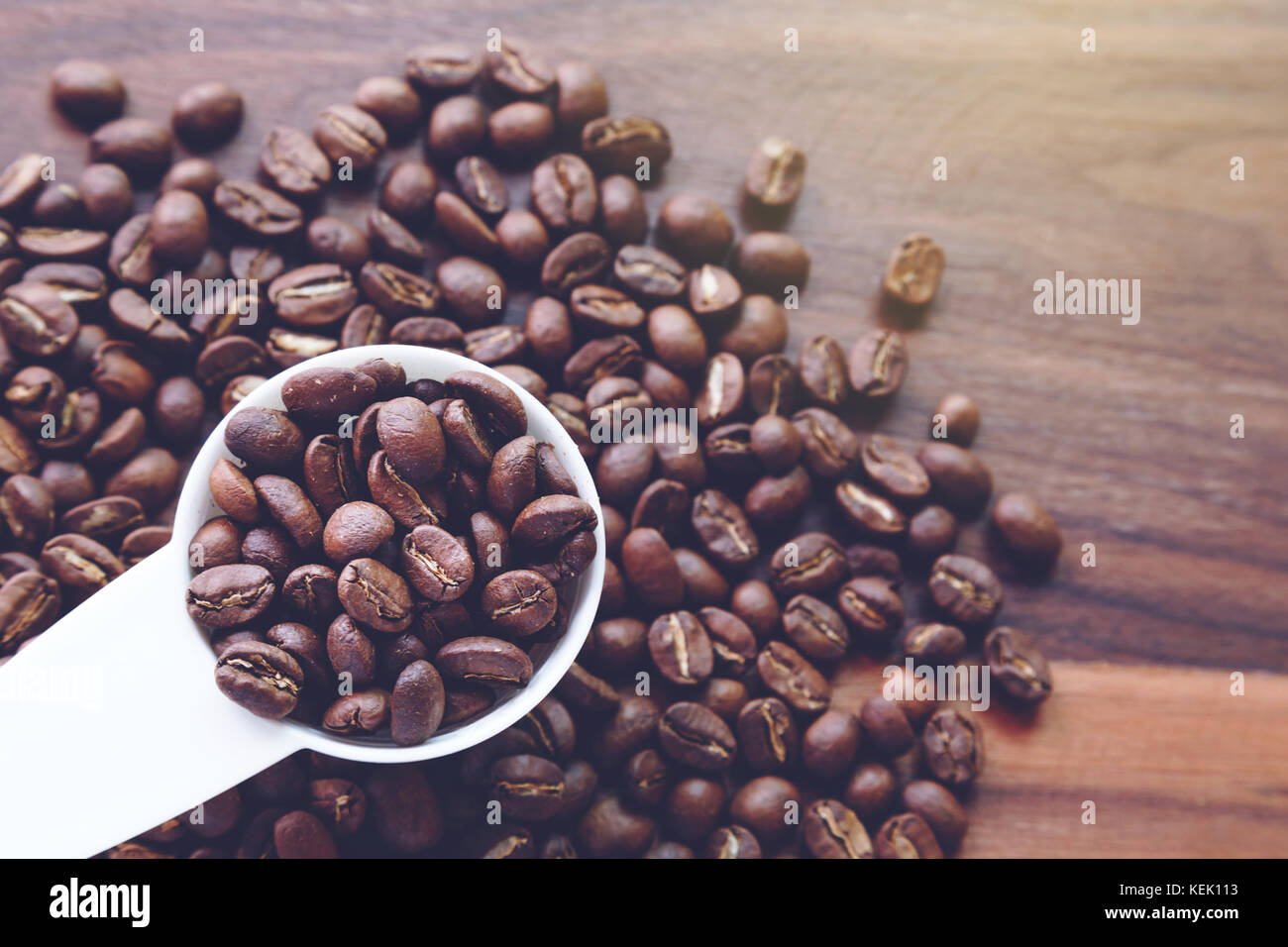 Dunkel geröstete Kaffee Bohnen in den weißen Plastiklöffel auf hölzernen Hintergrund bereit, um eine Tasse Kaffee zu machen. Stockfoto