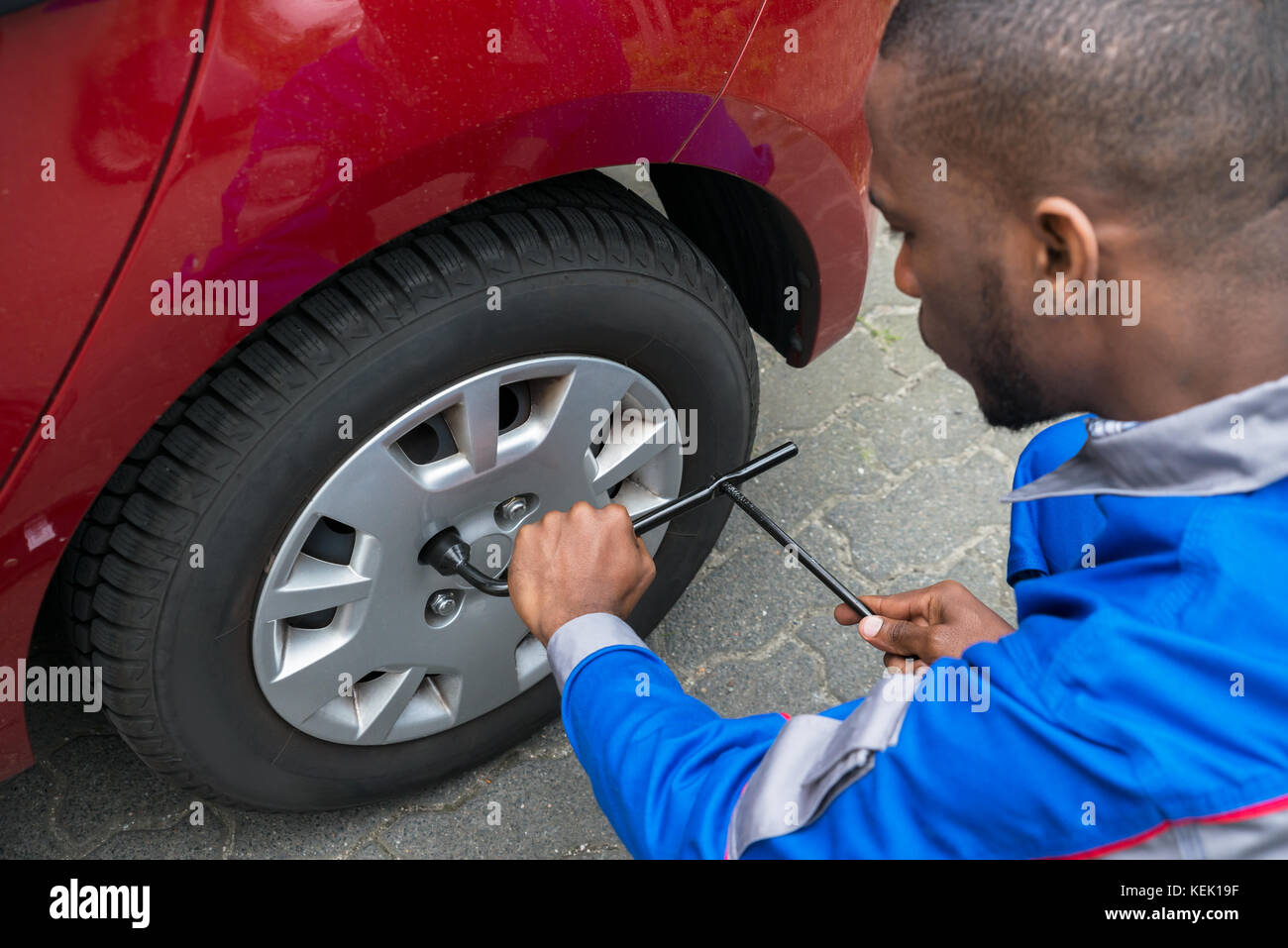 Junge afrikanische Mechaniker Reifenwechsel von einem roten Auto mit Schlüssel Stockfoto