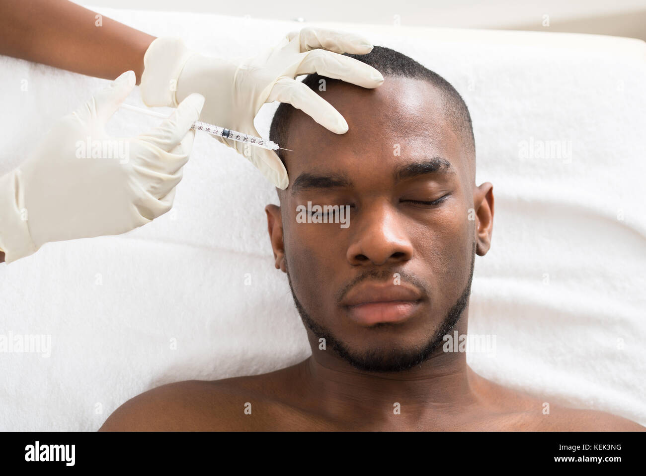 Nahaufnahme der Person Hand Spritzen Spritze auf Jungen afrikanischen Mann Gesicht Stockfoto