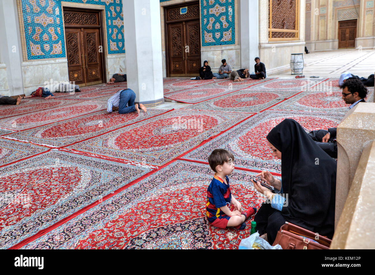 Shiraz, Iran - 19 April 2017: Eine junge muslimische Frau in einem islamischen Schleier sieht durch die Informationen auf Ihrem Smartphone, ein kleiner Junge sitzt neben ihm Stockfoto