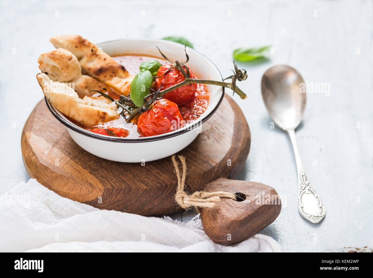 Italienische Tomaten, Knoblauch und Basilikum Suppe Pappa al pomodoro in Metallschale mit Brot auf rustikalen Holzbrett über hellblauen Hintergrund Stockfoto