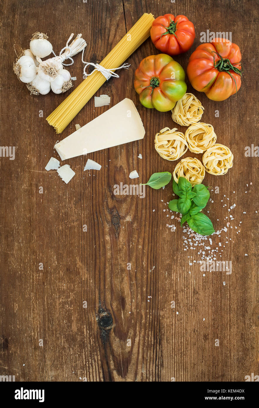 Zutaten zum Kochen Pasta Spaghetti, Tagliatelle, Knoblauch, Parmesan, Tomaten und frischem Basilikum auf rustikalen Holzmöbeln Hintergrund, Ansicht von oben, kopieren. Stockfoto