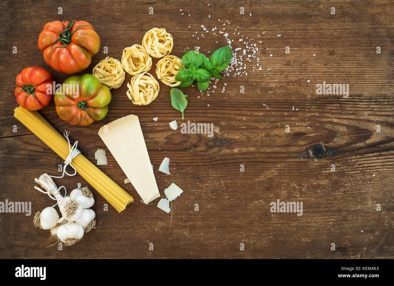 Zutaten zum Kochen Pasta Spaghetti, Tagliatelle, Knoblauch, Parmesan, Tomaten und frischem Basilikum auf rustikalen Holzmöbeln Hintergrund, Ansicht von oben, kopieren. Stockfoto