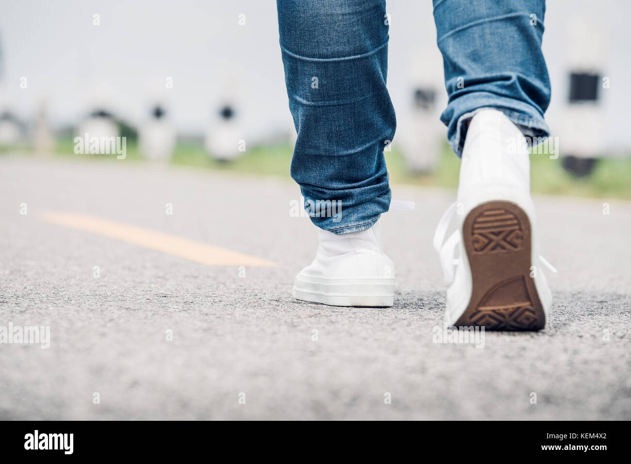 Nahaufnahme, Frau tragen Jean und weiße Sneaker vorwärts zu Fuß auf der Autobahn unterwegs in sonniger Tag, allein reisen oder Alleinreisende Konzept. Stockfoto