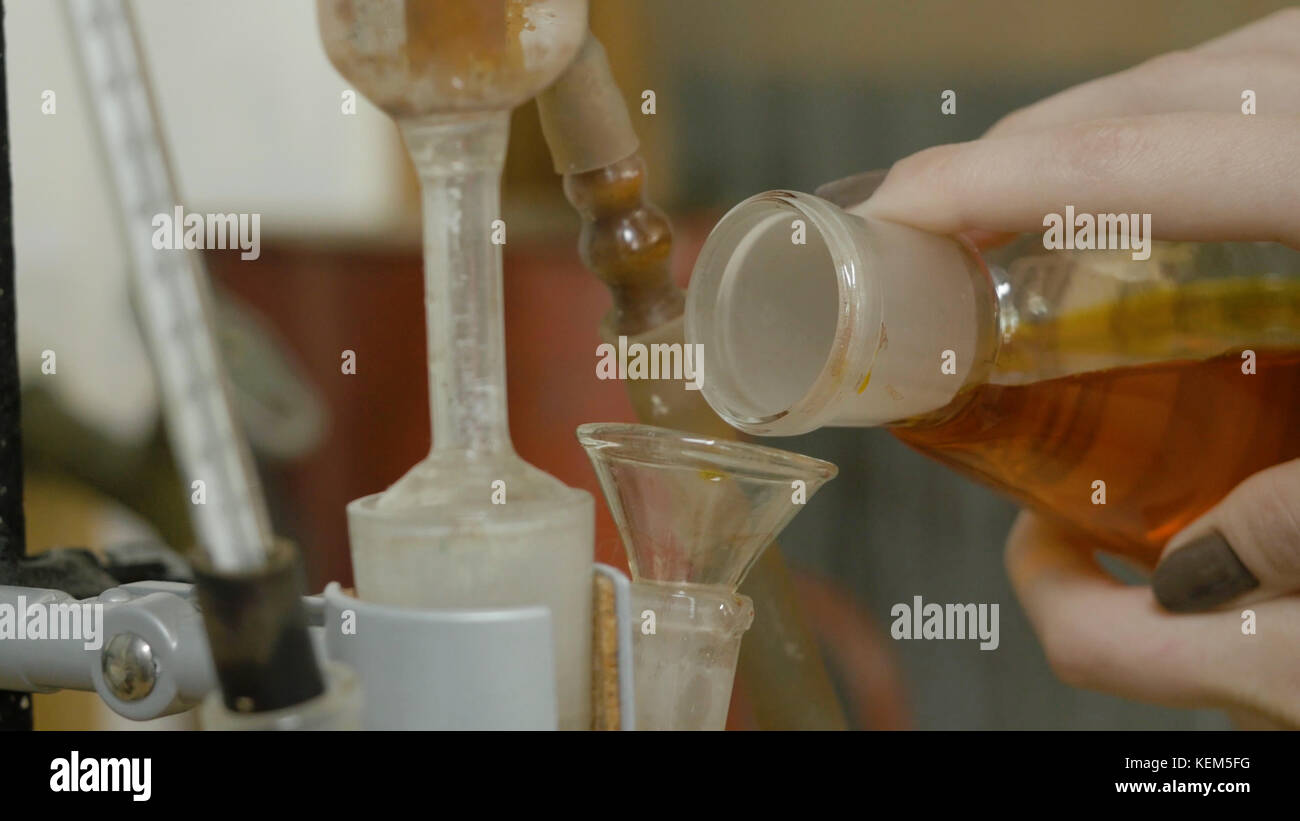 Chemisches Glas mit grüner Flüssigkeit, in ein rotes unter den Trichtern gegossen. Geben Sie mit der Hand rote gemischte Flüssigkeit in den Kolben. Ein Chemiker oder Medizinforscher fügt Chemikalien in einen erlenmeyerkolben für die chemische Reaktion hinzu Stockfoto