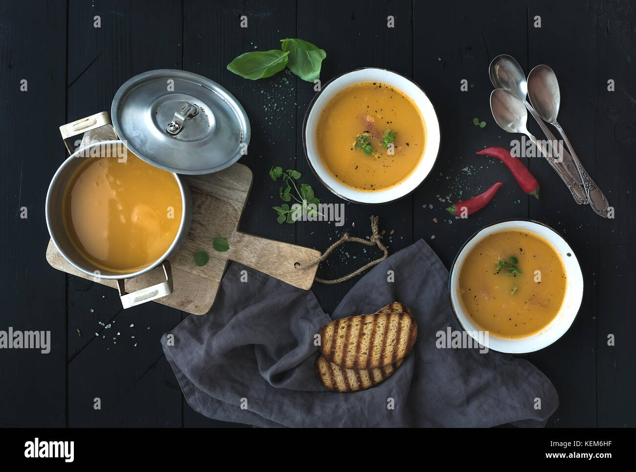 Rote Linsensuppe mit Gewürzen, Kräutern, Brot in einem rustikalen Metall Topf und Schüsseln, über dunklen Hintergrund, Ansicht von oben Stockfoto