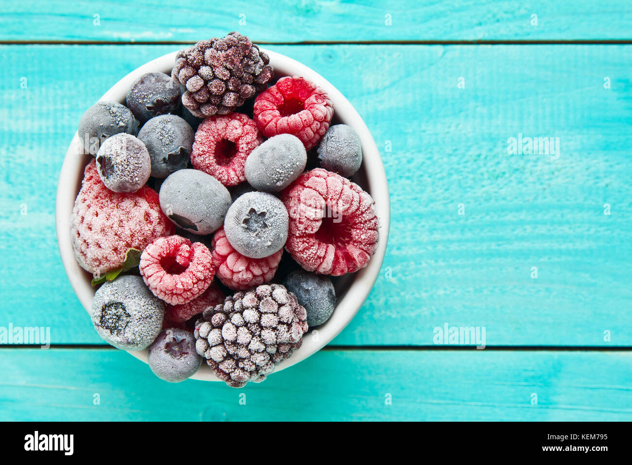 Verschiedene gemischte gefrorene Beeren in einer Schüssel auf blauem Hintergrund Stockfoto