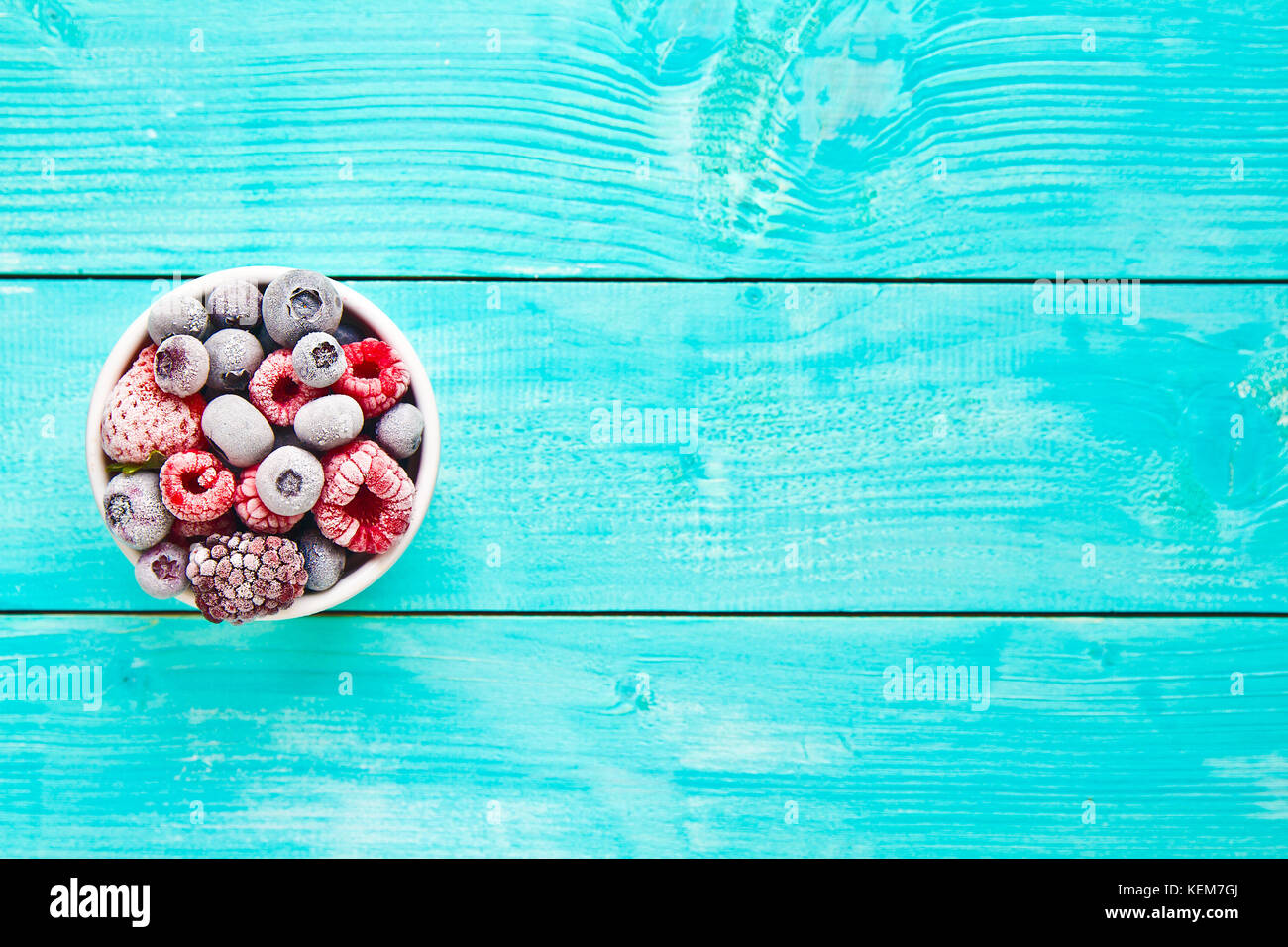 Verschiedene gemischte gefrorene Beeren in einer Schüssel auf blauem Hintergrund Stockfoto