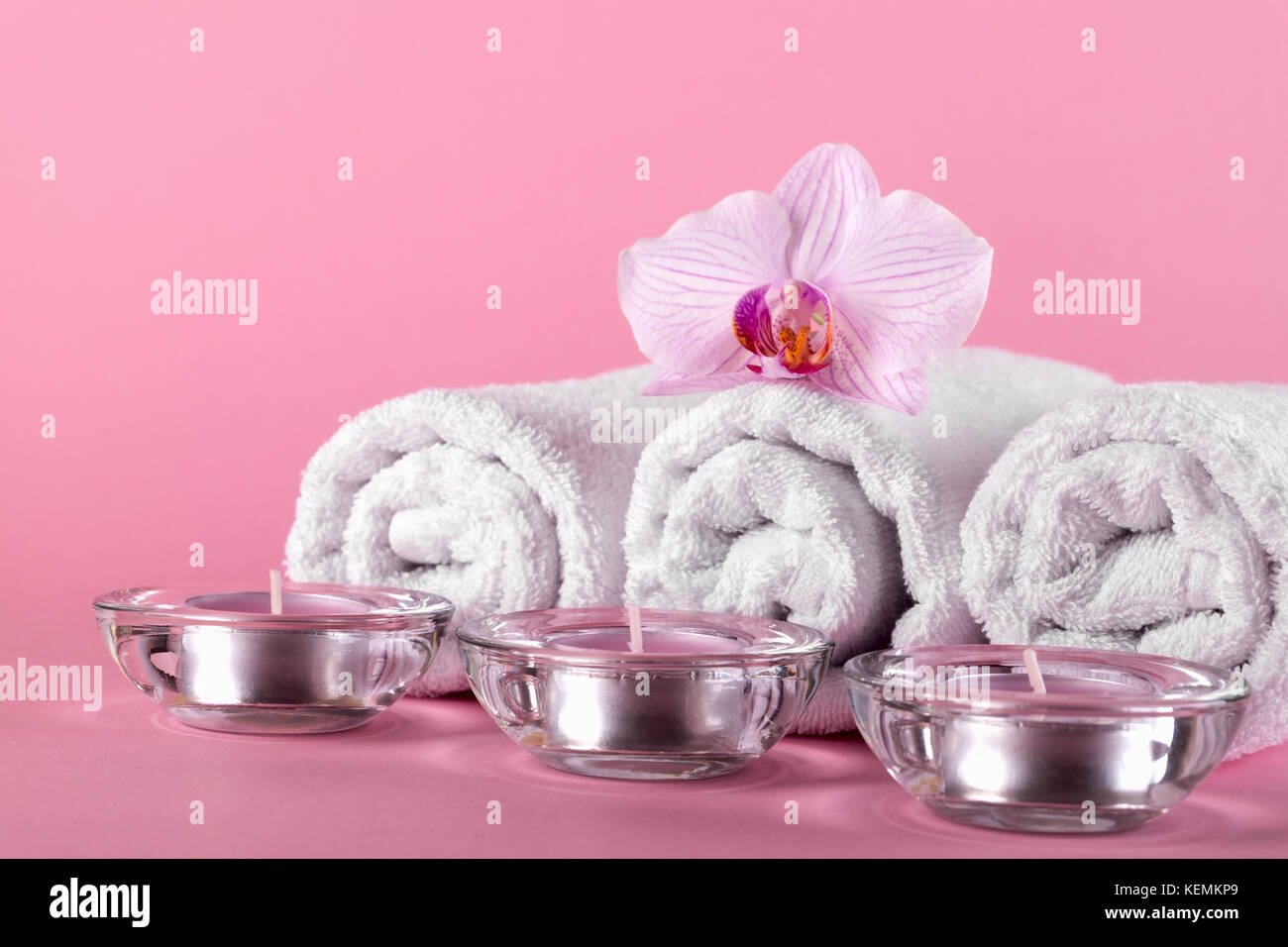 Handtücher, Kerzen und Orchidee Blumen für ein Spa Entspannung auf einem rosa Hintergrund Stockfoto