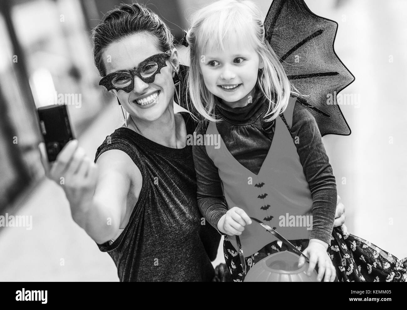 Trick oder Festlichkeit. Happy trendy Mutter und Kind in bat Kostüme zu Halloween in der Mall mit Digitalkamera unter selfie Stockfoto