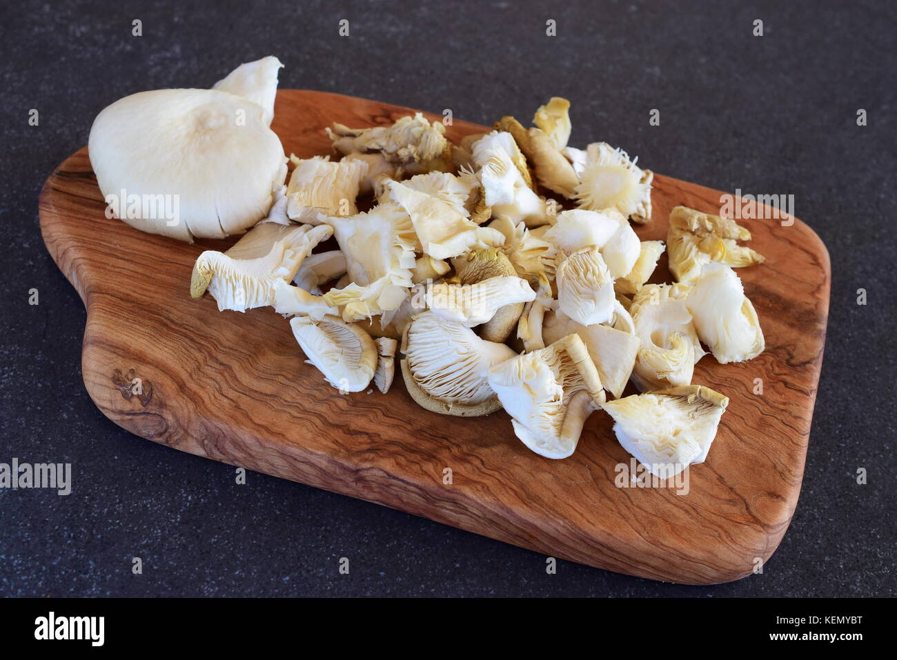 Frische Austernpilze in grosse Stücke auf einem olivenholz Schneidbrett auf einem grauen Abstrakt Hintergrund ausschneiden. Schritt für Schritt kochen Stockfoto