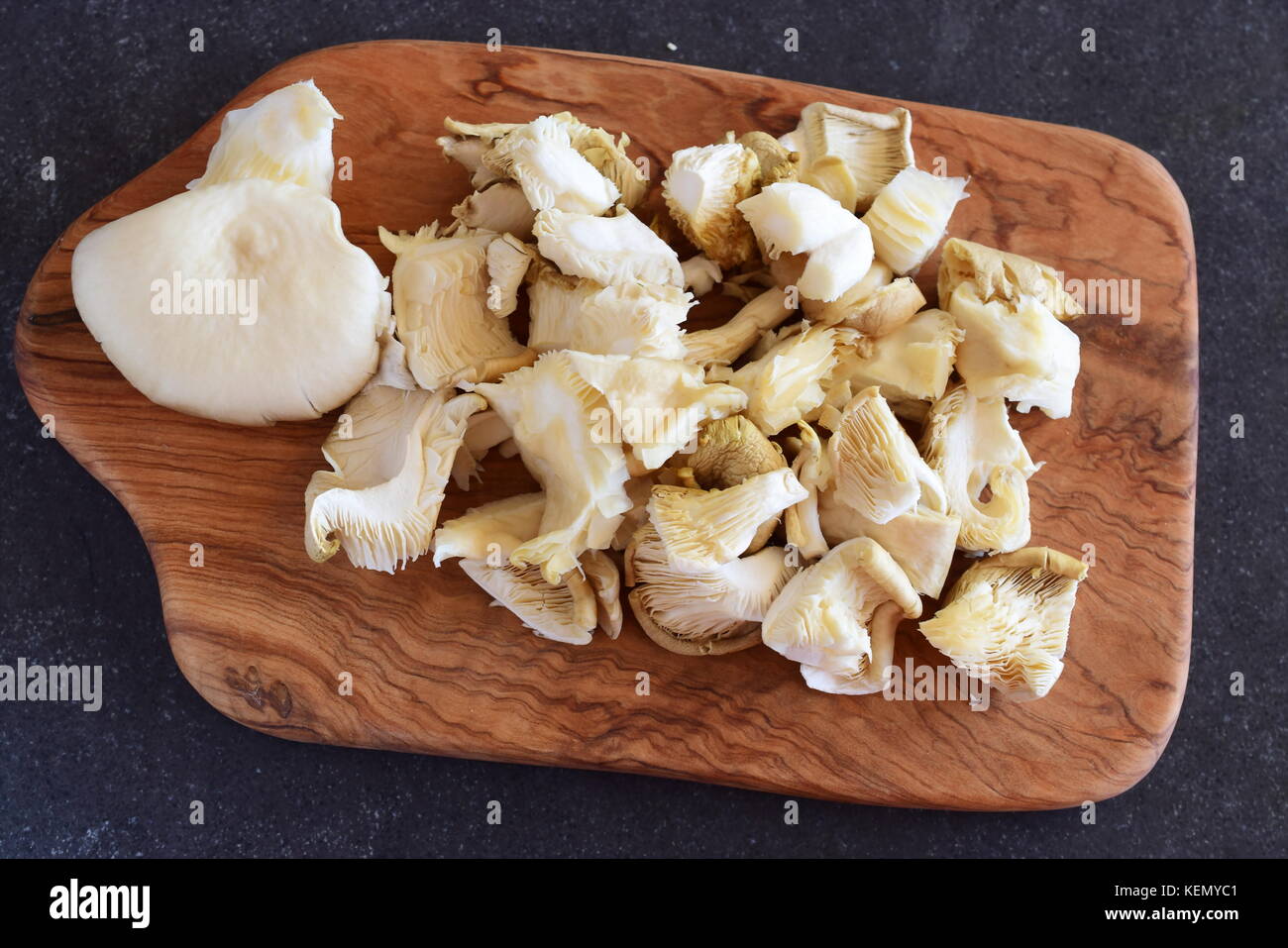 Frische Austernpilze in grosse Stücke auf einem olivenholz Schneidbrett auf einem grauen Abstrakt Hintergrund ausschneiden. Schritt für Schritt kochen Stockfoto