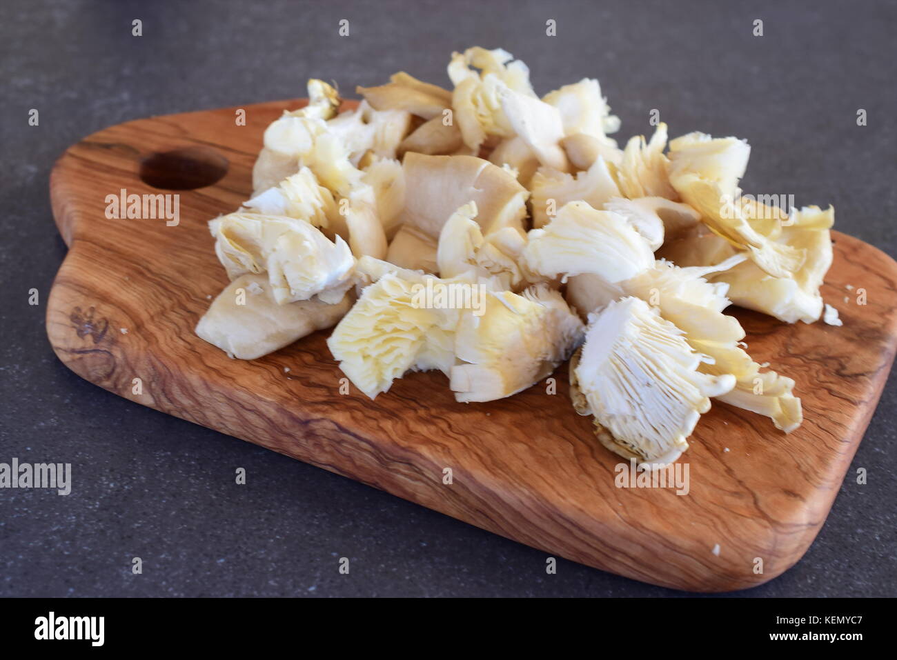 Frische Austernpilze in grosse Stücke auf einem olivenholz Schneidbrett auf einem grauen Abstrakt Hintergrund ausschneiden. Schritt für Schritt kochen Stockfoto