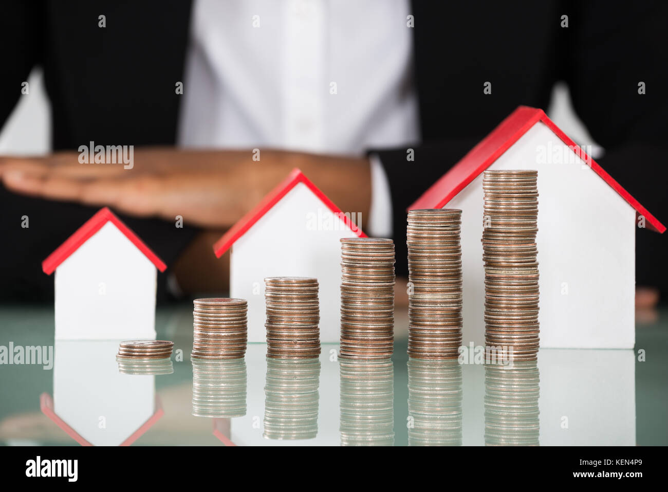 Nahaufnahme der Geschäftsfrau mit unterschiedlichen Größe des Hauses Modell und gestapelte Münzen auf Schreibtisch Stockfoto