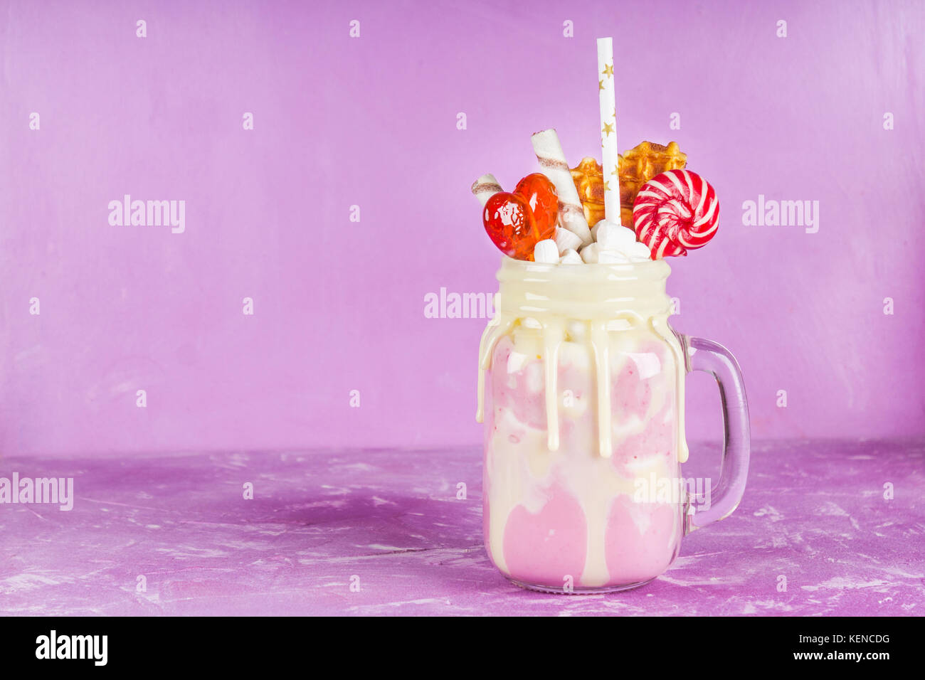 Freakshake von rosa Smoothie, Creme. monstershake mit Lutscher, Waffeln und Eibisch. extreme Milchshake in einem Marmeladenglas. rosa lila Hintergrund. Stockfoto