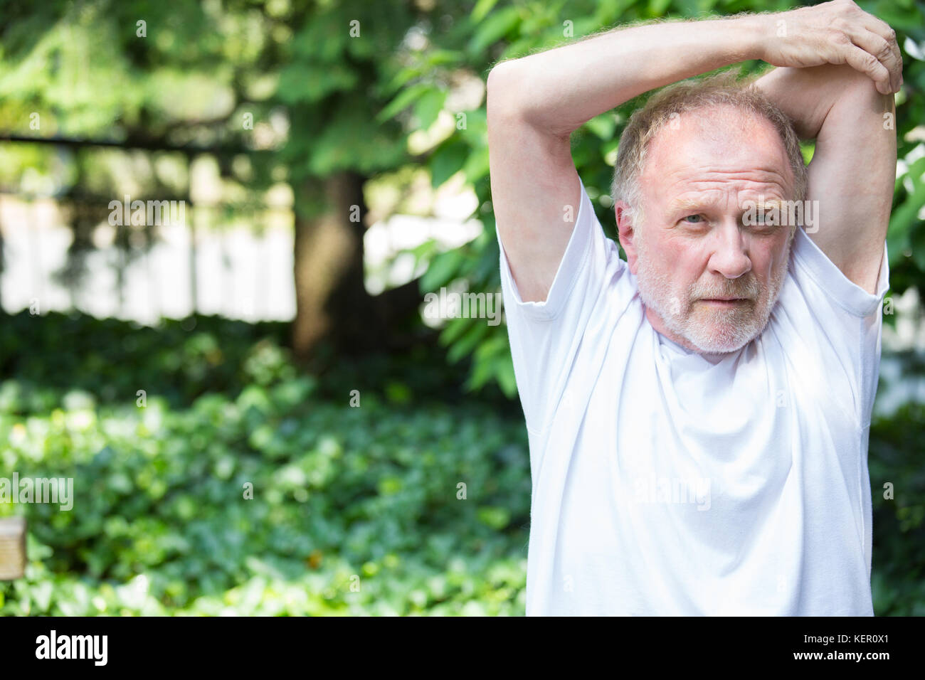 Closeup Portrait, Senior reifer Mann im weißen Hemd, Stretching Arms, isolierte grüne Bäume Hintergrund. Aufwärmen Stockfoto