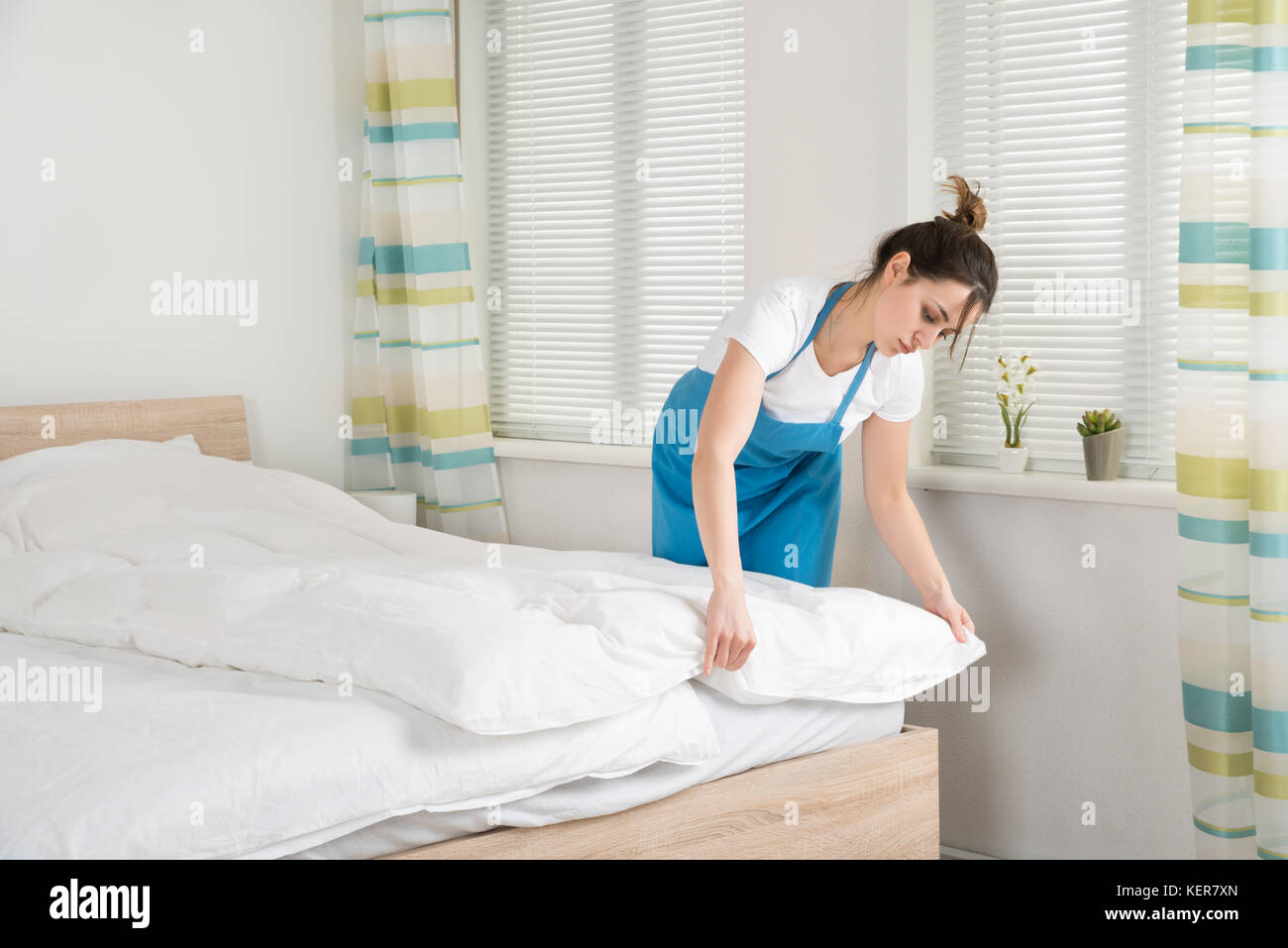 Junge weibliche Haushälterin, die die Bettlaken auf dem Bett im Zimmer Stockfoto