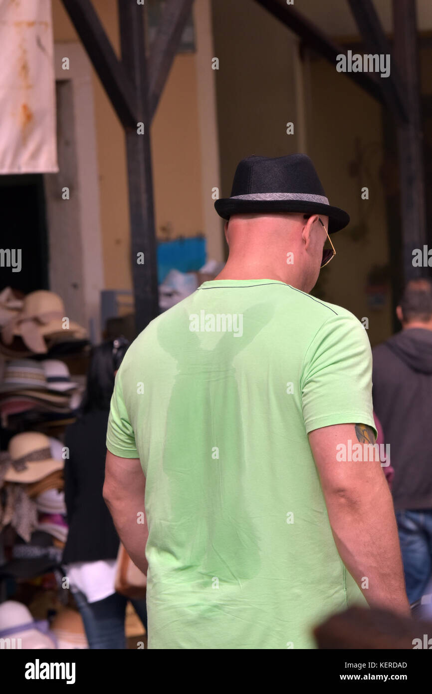Ein Mann mit Hut und Schwitzen stark durch sein Shirt mit Markierungen, wo sein Rucksack verlassen wurde Schweißflecken auf seinem Hemd. Stockfoto