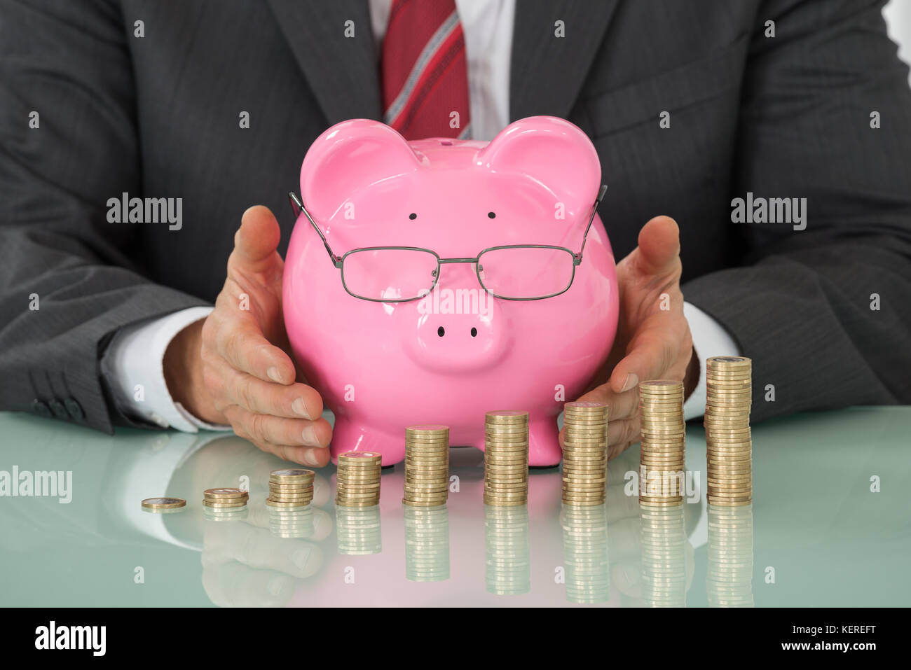 Nahaufnahme der Geschäftsmann Hand abdecken Sparschwein mit gestapelten Münzen am Schreibtisch Stockfoto Nahaufnahme der Geschäftsmann Hand abdecken Sparschwein mit gestapelten Münzen am Schreibtisch Stockfoto