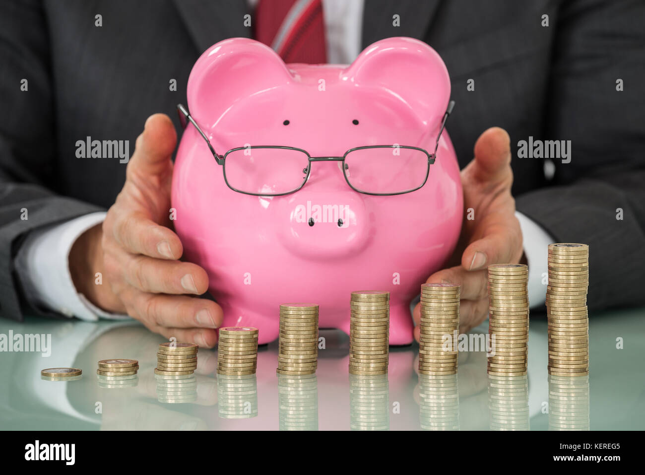 Nahaufnahme der Geschäftsmann Hand abdecken Sparschwein mit gestapelten Münzen am Schreibtisch Stockfoto Nahaufnahme der Geschäftsmann Hand abdecken Sparschwein mit gestapelten Münzen am Schreibtisch Stockfoto
