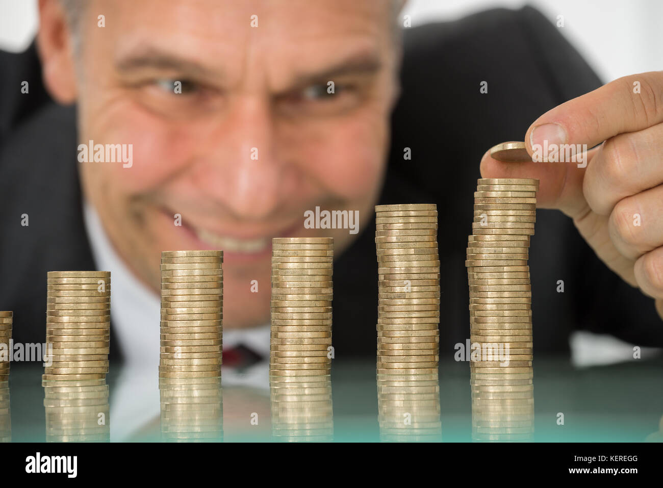 Reifen glücklich Geschäftsmann Inverkehrbringen Münze über Stapel von Münzen am Schreibtisch Stockfoto