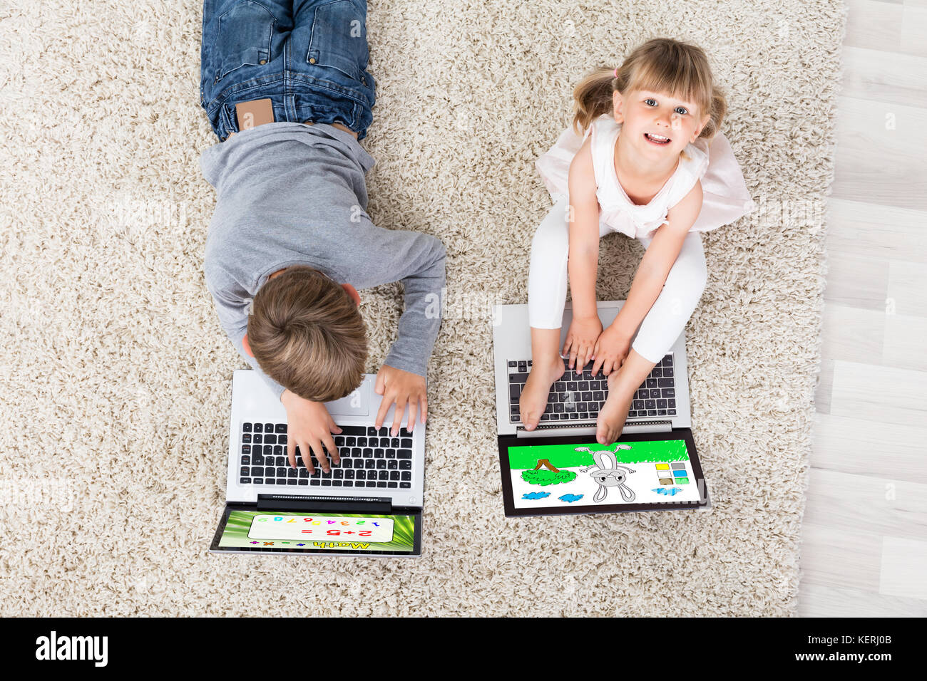 Zwei Kinder mit einem Laptop auf dem Teppich zu Hause Stockfoto