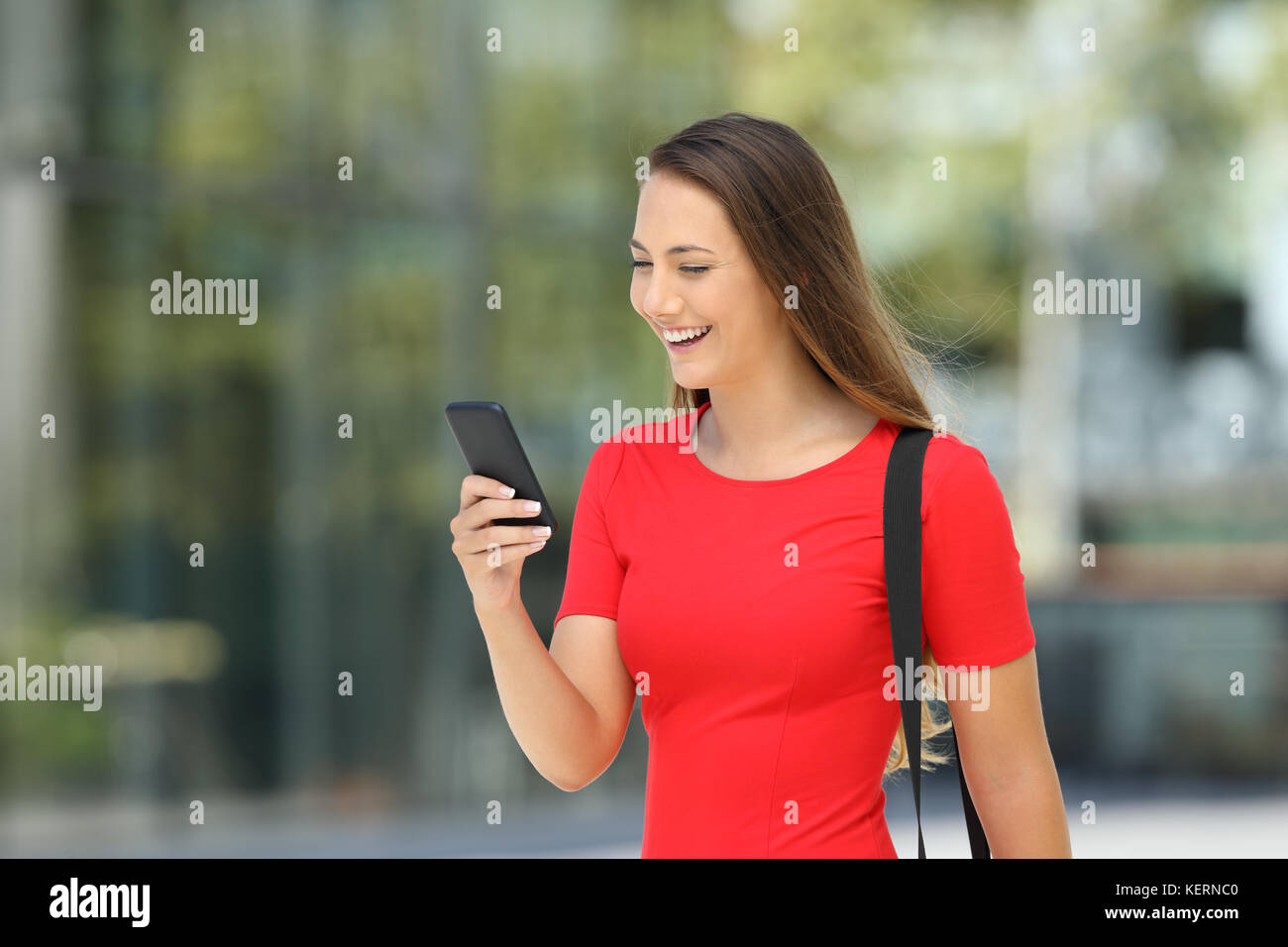 Einzelne Unternehmer trägt ein rotes Kleid lesen Online Inhalte in ein Mobiltelefon zu Fuß auf der Straße Stockfoto