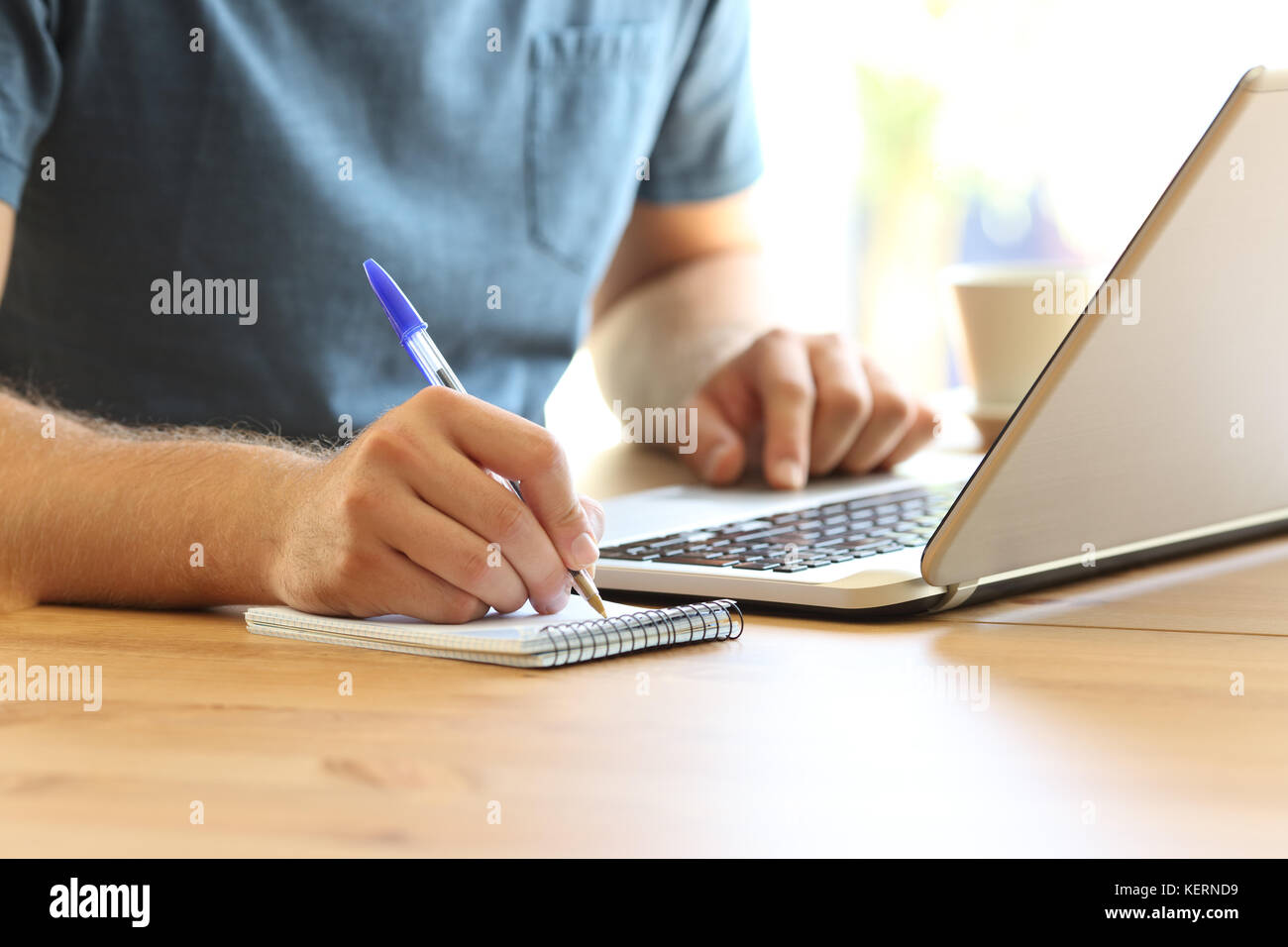 Nahaufnahme eines Mannes Hand auf der Linie von Notizen in ein Notebook und ein Laptop auf einem Desktop Stockfoto