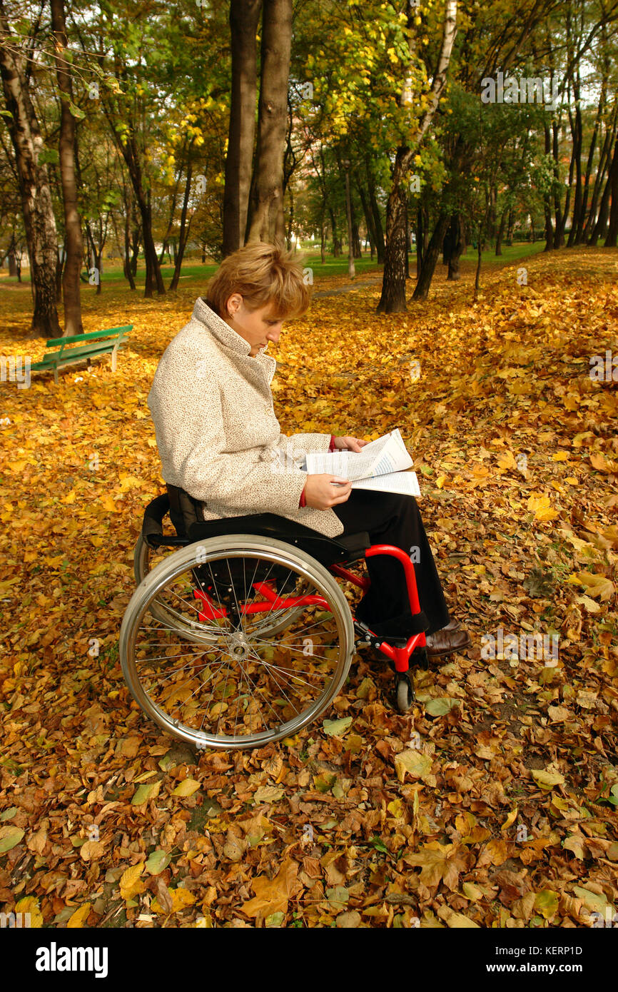 Frau im Rollstuhl das Lesen einer Zeitschrift in den Park im Herbst Zeit Stockfoto