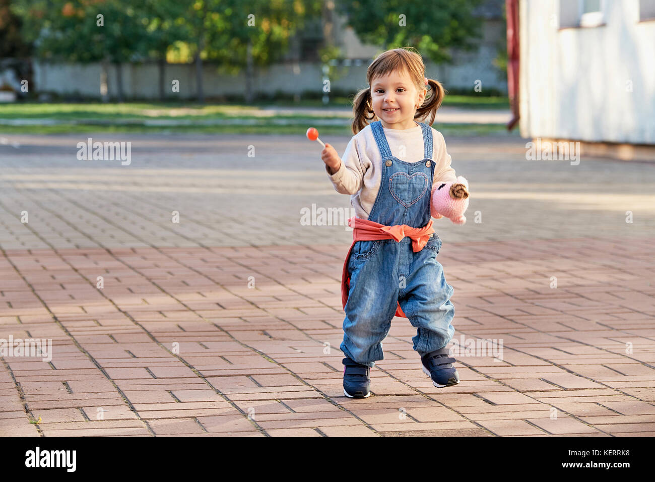 Lustige kleine Mädchen vor Freude hüpfend. Ein junges Kind in Jeans Overalls Stockfoto
