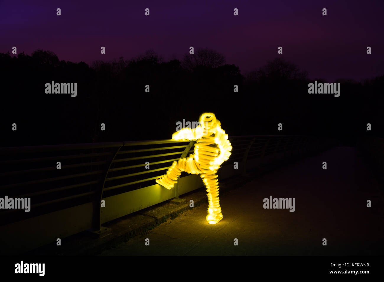 Ungeklärte, geheimnisvolle, glühende Figur (wie eine Mumie), isoliert im Freien auf einer Brücke in der Dunkelheit. Leichte Nachtmalerei. Stockfoto