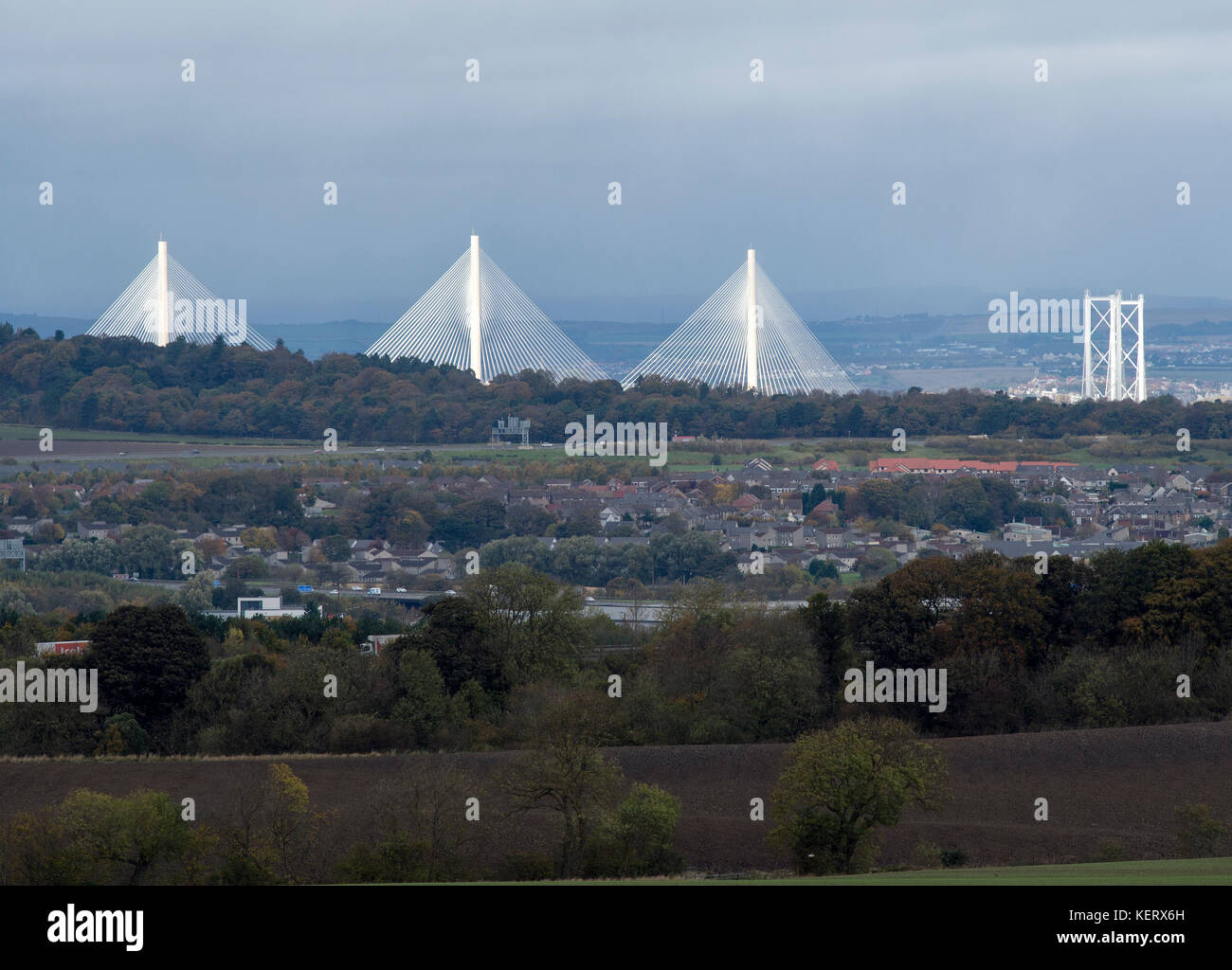 Ein Blick auf die neuen Queensferry Crossing und Forth Road Bridge von der Sonne mit Kirkliston Dorf im Vordergrund auf ein stumpfes Oktober Tag beleuchtet. Stockfoto